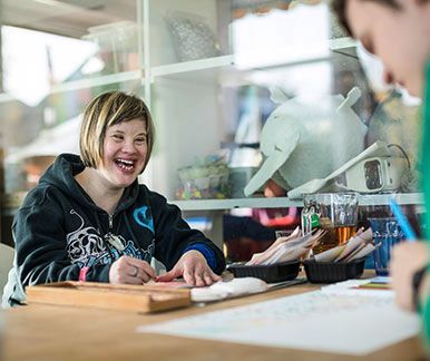 Jeune femme avec le syndrome de Down riant pendant qu’elle dessine