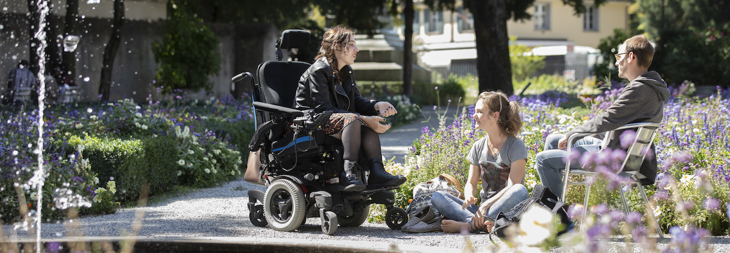 Trois jeunes, dont un en fauteuil roulant, parlent à l'extérieur