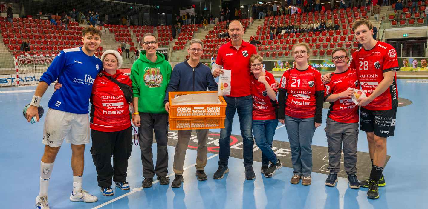 Un gruppo di persone è in posa con una cassetta di Grittibänz sul parquet della Axa Arena di Winterthur.