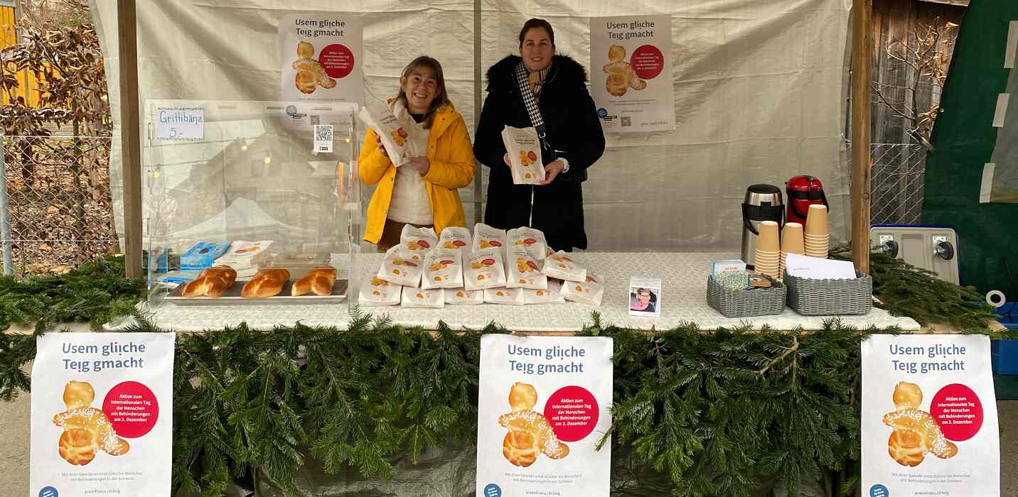 Zwei Personen an einem Stand mit inklusiven Grittibänzen, der mit Tannenzweigen geschmückt ist