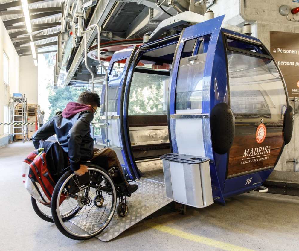Une personne en chaise roulante entre dans une télécabine par une rampe.