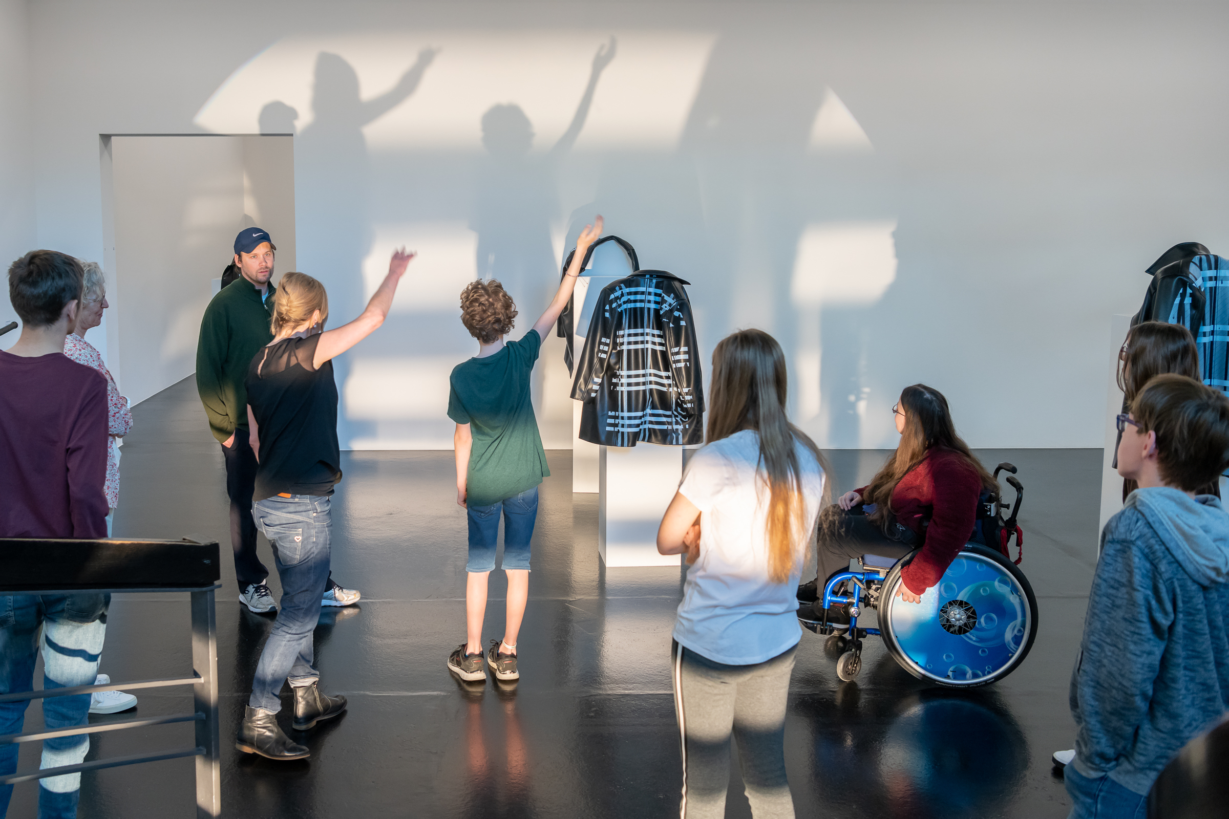 Workshop Situation im Aargauer Kunsthaus. Jugendliche mit und ohne Rollstuhl betrachten ein Kunstwerk in Form einer Jacke und machen Schattenfiguren an die Wand Ferienworkshop_Fruehling22_FC_UllmannPhotography_WEB-30.jpg